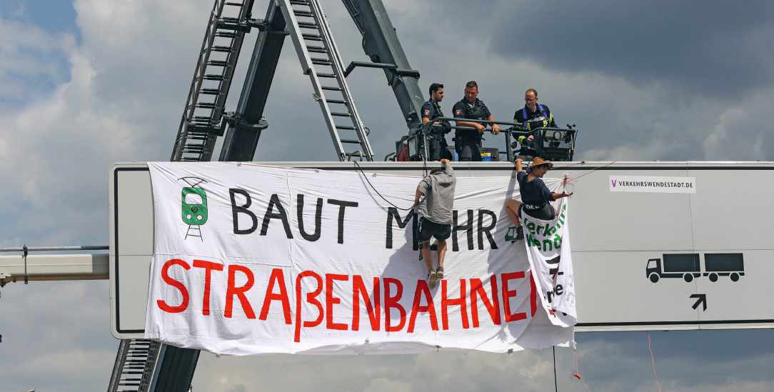 Verkehrswendestadt Wolfsburg? Polizisten versuchen, Klimaaktivisten von einer Schilderbrücke an der Lieferzufahrt von VW zu entfernen(Foto: PA / DPA / Bodo Marks)